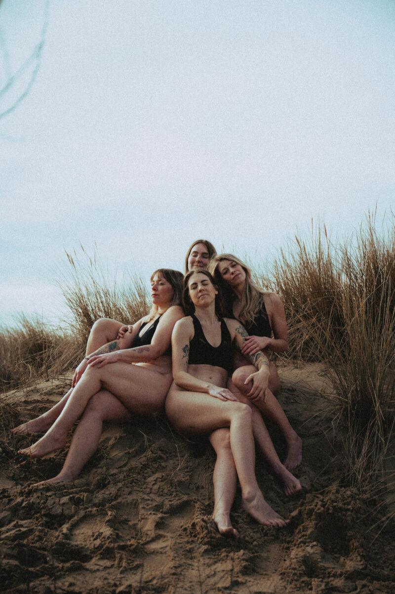 Group of 4 woman sitting in dunes wearing activewear
